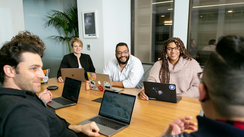 Four people working on laptops listening to a colleague